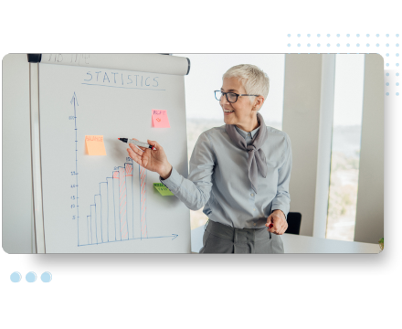 A person with short gray hair and glasses is smiling while presenting a bar graph on a flip chart, with sticky notes labeled Statistics highlighting analytics and data-driven strategies.