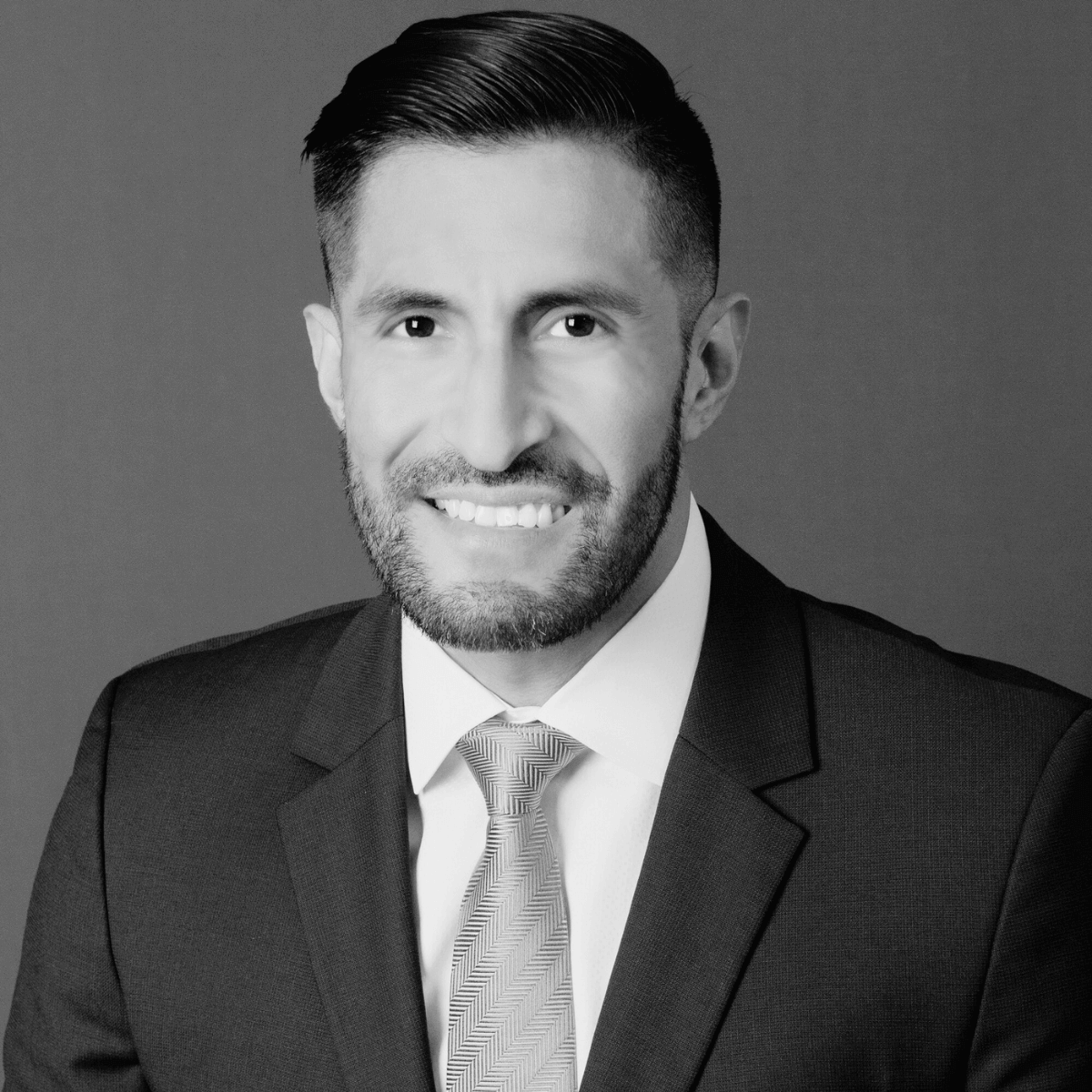 A smiling man in a suit and tie poses for a professional headshot. The black-and-white image exudes a confident and approachable tone.
