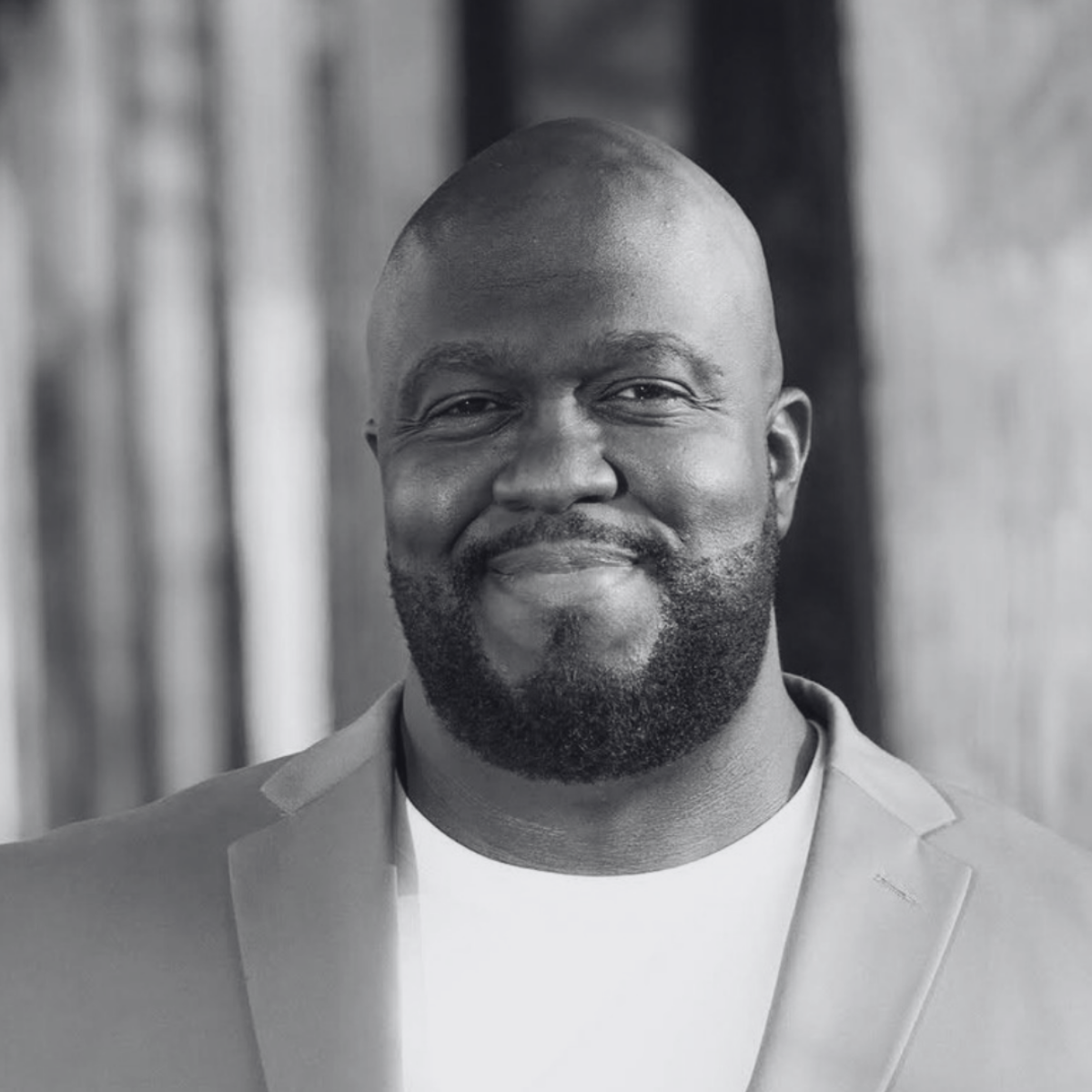 Black and white portrait of a man with short, styled hair and a subtle beard, wearing a patterned shirt. He gazes directly, conveying a confident tone.